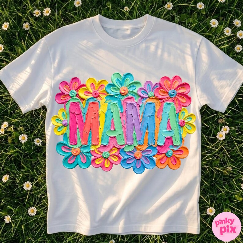 May include: White t-shirt with the word "MAMA" in colorful, textured letters, surrounded by vibrant, multi-colored flowers. The design features shades of pink, orange, yellow, blue, and green, creating a cheerful and eye-catching look.
