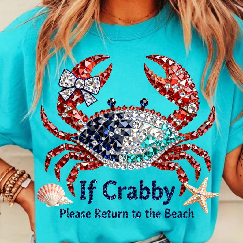 May include: A turquoise t-shirt features a crab design made of red, white, blue, and clear rhinestones. The crab has a bow and the text "If Crabby Please Return to the Beach". A seashell and starfish are also on the shirt.