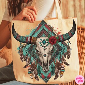 May include: Cream-coloured tote bag with a detailed illustration of a bull skull with long black horns. The design includes turquoise, red, and brown accents, a red rose, and hanging feathers, evoking a bohemian or Southwestern theme.