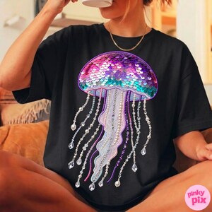 May include: Black t-shirt featuring a colorful jellyfish design. The jellyfish has a sequined dome in shades of pink, purple, and teal, with beaded and crystal-like strands. The design is centered on the shirt.