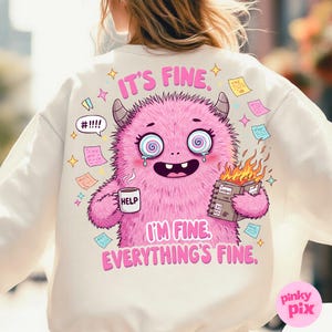 May include: A white sweatshirt with a pink monster graphic and the text "It's fine. I'm fine. Everything's fine." The monster has a distressed look with spiral eyes and is holding a cup that says "Help" and a notebook with flames coming out of it.