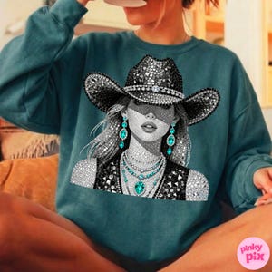 May include: Teal-colored sweatshirt featuring a rhinestone-studded cowgirl graphic. The graphic includes a black cowboy hat, jewelry, and a vest. The design is in black, white, and teal. The sweatshirt is a comfortable, casual style.