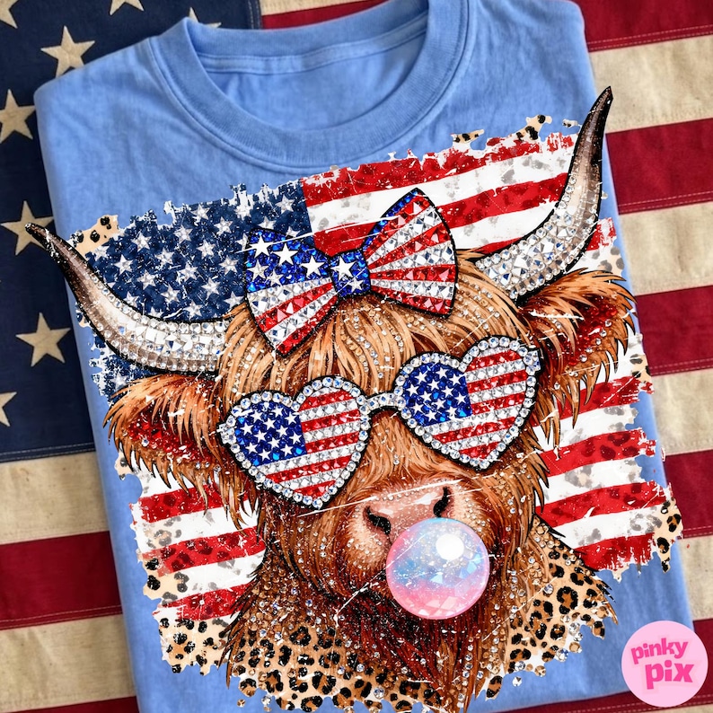 May include: Light blue t-shirt featuring a brown Highland cow with rhinestone accents, heart-shaped sunglasses, and a bow, all decorated with the American flag. The cow is blowing a bubble and has a leopard print collar. The shirt is on an American flag background.