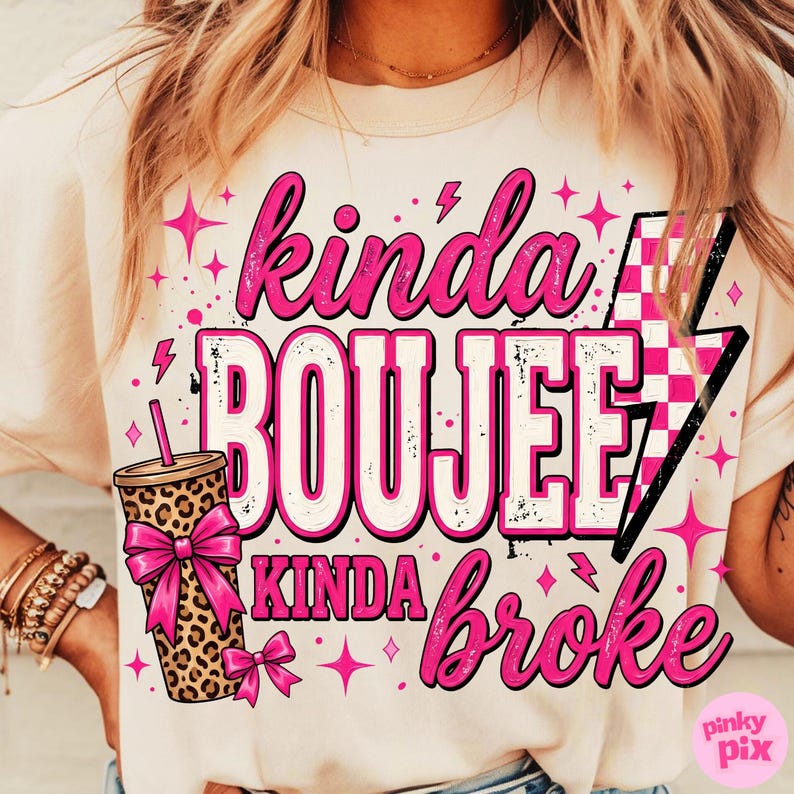 May include: A cream-colored t-shirt featuring a graphic print with the text "kinda BOUJEE kinda broke". The design includes a leopard print tumbler with a bright pink bow, a pink and white checkered lightning bolt, and various pink star icons.