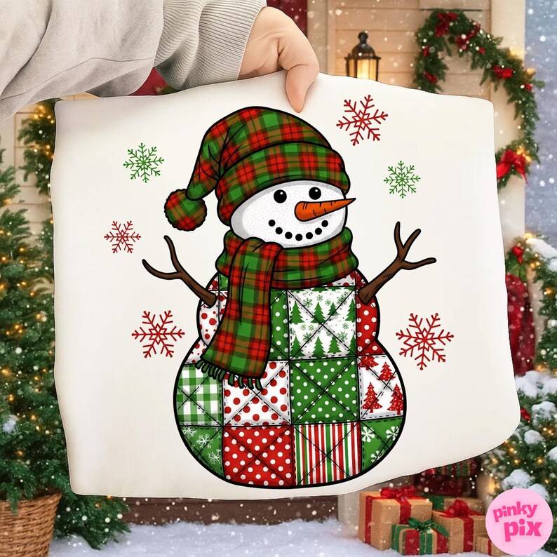 May include: A white pillow featuring a snowman design. The snowman wears a plaid hat and scarf in red and green. The body is made of patchwork squares in red, green, and white. Decorative snowflakes surround the snowman.
