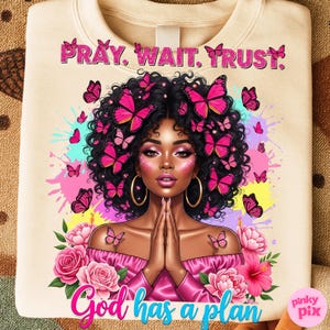 May include: Cream-coloured sweatshirt with a colourful illustration of a woman adorned with butterflies. The text "PRAY. WAIT. TRUST." is at the top, and "God has a plan" is at the bottom. Pink and blue accents are used in the design.