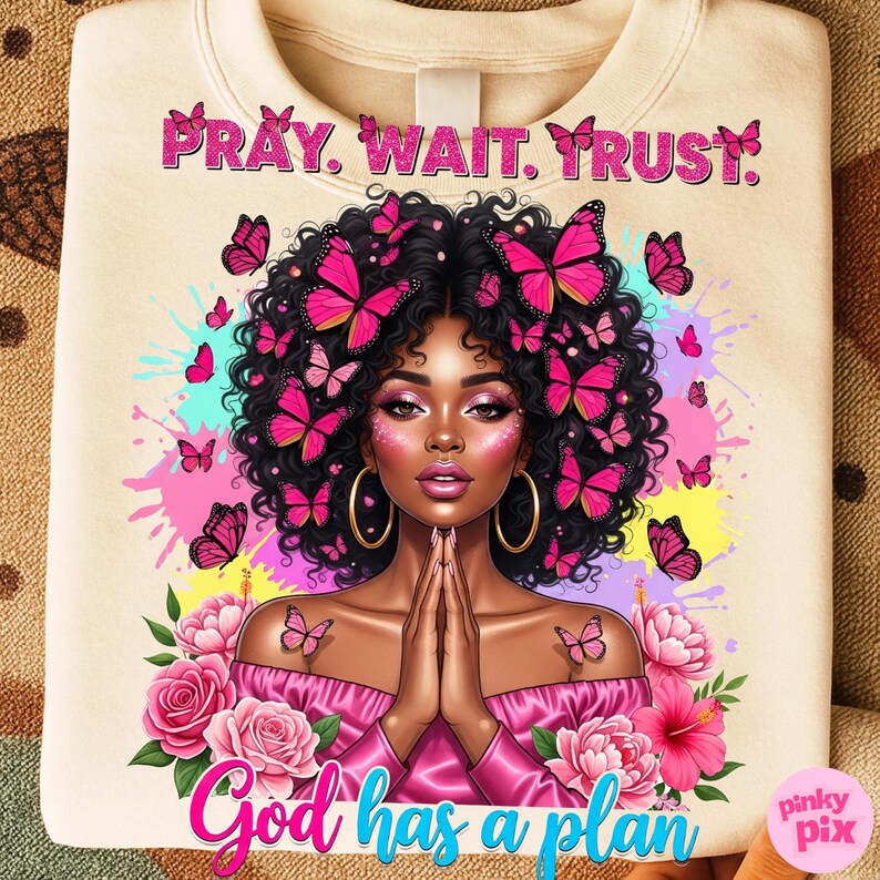 May include: Cream-coloured sweatshirt with a colourful illustration of a woman adorned with butterflies. The text "PRAY. WAIT. TRUST." is at the top, and "God has a plan" is at the bottom. Pink and blue accents are used in the design.