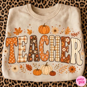 May include: A beige crewneck sweatshirt featuring the word TEACHER in large, patterned letters filled with orange, brown, and white floral, plaid, and polka dot designs. The graphic is surrounded by illustrations of pumpkins and autumn leaves.