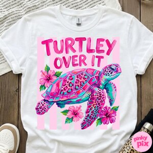 May include: White t-shirt with a colorful graphic of a sea turtle and the text "Turtley Over It" in pink. The turtle has a pink and teal shell with a leopard print design, surrounded by pink flowers.