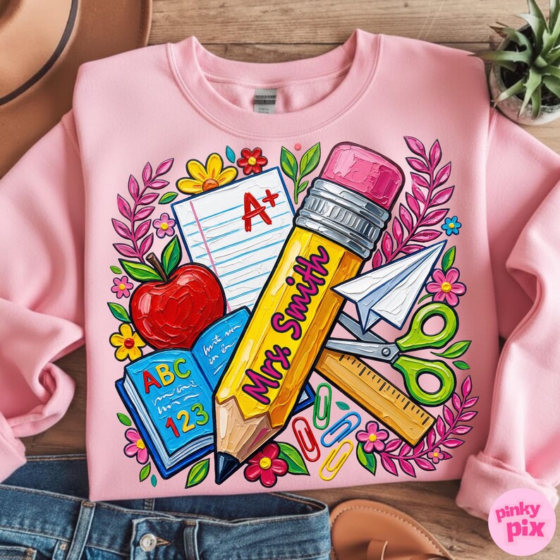 Pu&ograve; includere: Felpa rosa con grafica a tema insegnante. Il design include una grande matita gialla con la scritta "Mrs. Smith", una mela, un libro aperto e materiale scolastico. Il design &egrave; circondato da fiori e foglie.