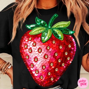 K&ouml;nnte beinhalten: Schwarzes T-Shirt mit einem gro&szlig;en, paillettenbesetzten Erdbeer-Design. Die Erdbeere ist rot und rosa mit gr&uuml;nen Bl&auml;ttern und Stiel und mit klaren Strasssteinen verziert. Das Design ist auf dem T-Shirt zentriert.