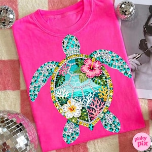 May include: A bright pink t-shirt featuring a bejeweled sea turtle design. The turtle has turquoise, yellow, and clear gem accents, with a turquoise and white ocean scene on its shell. Pink and white hibiscus flowers and coral complete the design.