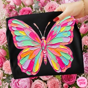 May include: Black tote bag featuring a vibrant, textured butterfly design. The butterfly is rendered in a palette of pink, green, yellow, and orange hues. The image is set against a backdrop of pink roses and the text "pinky pix".