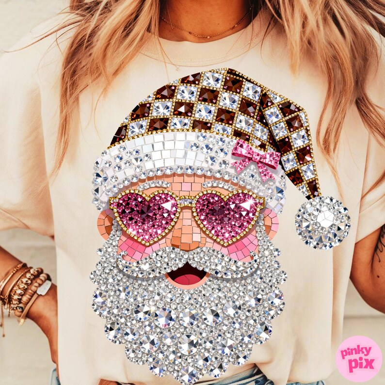 May include: A beige t-shirt featuring a graphic of a Santa Claus face composed of sparkling rhinestones. The design includes a brown and white checkered hat with a pink bow, heart-shaped pink sunglasses, and a large, textured white beard.