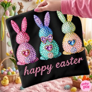 May include: Black tote bag featuring three beaded Easter bunnies in pink, blue, and yellow, each with a heart-shaped gem. The words "happy easter" are written in pink script. The bag is held up by a person.