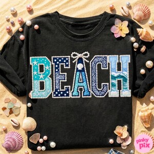 May include: Black long-sleeve shirt with the word "BEACH" in a patchwork design. The letters are in shades of blue and white, with star, polka dot, and wave patterns. The shirt is decorated with pearls, seashells, and flowers.