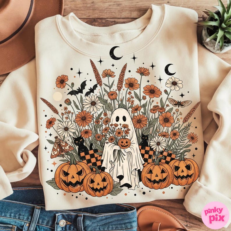 May include: Cream-coloured sweatshirt with a Halloween graphic. The design shows a ghost holding a pumpkin, surrounded by orange flowers, pumpkins, black cats, bats, and crescent moons. The graphic has a vintage, whimsical style.