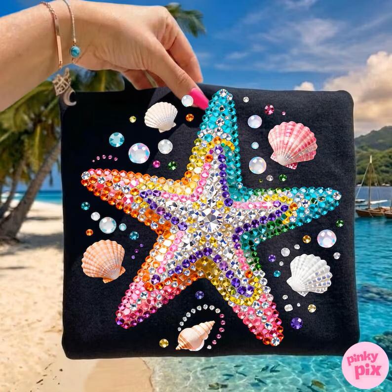 May include: Black square-shaped item with a large, colorful, bejeweled starfish design. The starfish is adorned with a variety of gems in shades of pink, yellow, blue, and purple. Scattered around the starfish are seashells and clear, sparkling bubbles.