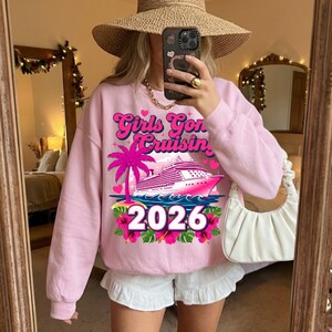 May include: Pink sweatshirt with the text "Girls Gone Cruisin' 2026" featuring a cruise ship, palm tree, and floral accents. The design is in shades of pink and white. The sweatshirt is long-sleeved.