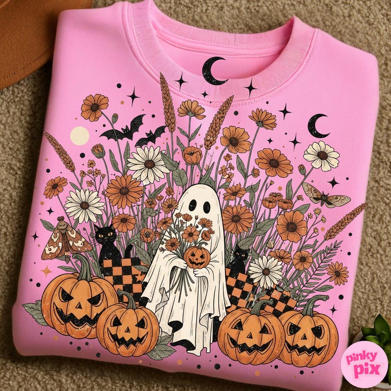 May include: Pink sweatshirt with a Halloween design. The graphic features a ghost holding a pumpkin and flowers, surrounded by pumpkins, black cats, and floral elements. The design includes moons, stars, and bats.