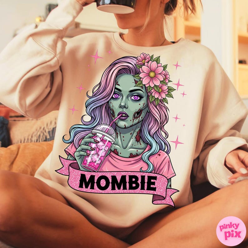 May include: Beige sweatshirt featuring a zombie graphic with pink and purple hair, holding a pink drink. The graphic includes the word "MOMBIE" on a pink banner, with pink star accents.