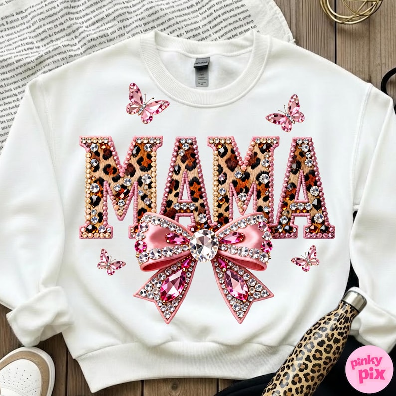 May include: White sweatshirt with the word "MAMA" in leopard print, embellished with rhinestones. A pink bow with rhinestones and butterflies are also featured. The sweatshirt is a casual, everyday wear item.
