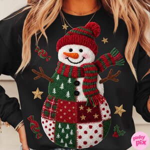 May include: Black sweatshirt featuring a snowman design. The snowman has a red and green striped hat and scarf, a carrot nose, and a patchwork body with red, green, and white patterns. Gold stars and candy accents are scattered around the snowman.