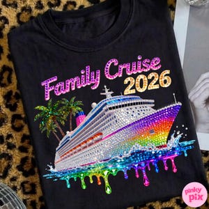 Op de afbeelding: Zwart T-shirt met een cruiseschipontwerp. Het schip is versierd met strass-steentjes en heeft een regenboogkleurige boeg. De tekst "Family Cruise 2026" wordt in glinsterende letters boven het schip weergegeven. Palmbomen staan aan de linkerkant.