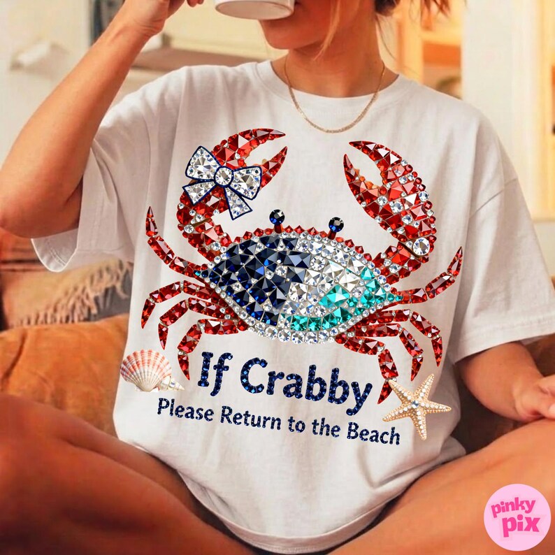 May include: White t-shirt featuring a crab design with red, blue, and clear crystal accents. The crab has a bow on one claw. Text on the shirt reads "If Crabby, Please Return to the Beach". A seashell and starfish are also on the shirt.