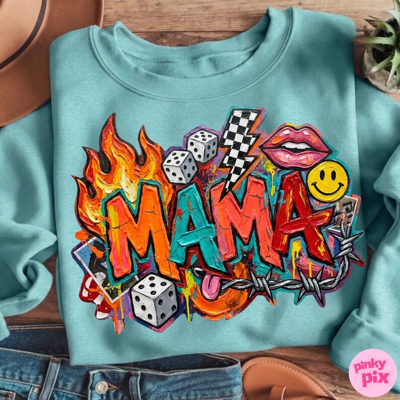 May include: A light blue sweatshirt with a colorful graffiti-style design. The word "MAMA" is prominently displayed, surrounded by flames, dice, a lightning bolt, lips, a smiley face, and barbed wire. The design is vibrant and eye-catching.