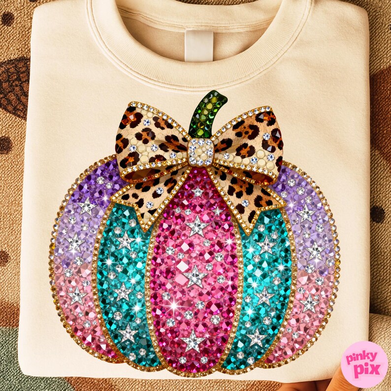 Op de afbeelding: Een cr&egrave;mekleurig sweatshirt met een grote, centrale afbeelding van een pompoen versierd met veelkleurige strass-steentjes in roze, turquoise en paarse tinten, geaccentueerd met zilveren stervormen en een strik met luipaardprint.