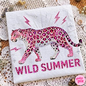 May include: White t-shirt featuring a pink leopard design with rhinestone accents. The leopard is surrounded by pink lightning bolts and stars. The words "WILD SUMMER" are printed in pink at the bottom.