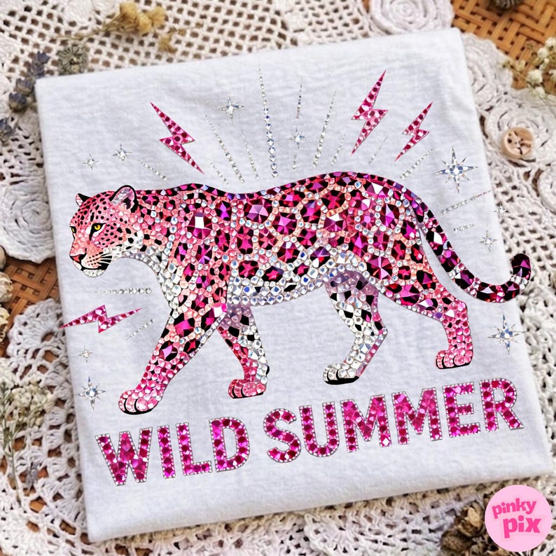 May include: White t-shirt featuring a pink leopard design with rhinestone accents. The leopard is surrounded by pink lightning bolts and stars. The words "WILD SUMMER" are printed in pink at the bottom.