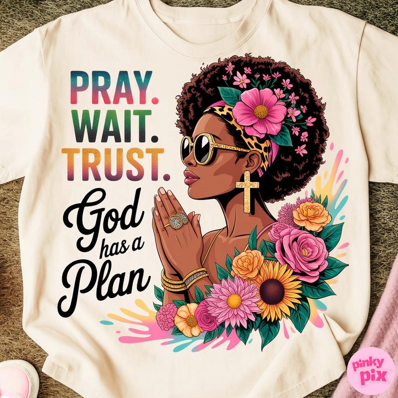 May include: Cream-colored t-shirt featuring a graphic of a woman with sunglasses, a cross earring, and floral accents. The text reads "PRAY. WAIT. TRUST. God has a Plan" in colorful lettering. The design includes a leopard print headband.