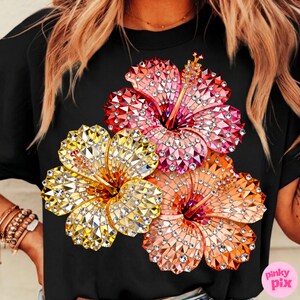 May include: Black t-shirt featuring a vibrant floral design. The design showcases three hibiscus flowers in shades of yellow, pink, and orange, embellished with sparkling details. The flowers are arranged on the front of the shirt.