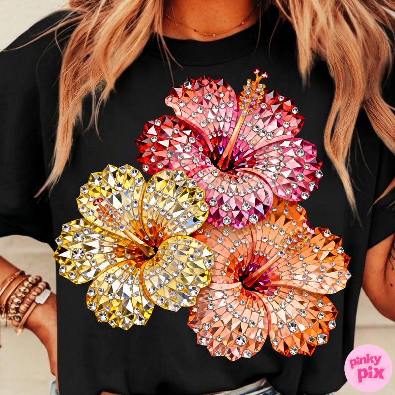May include: Black t-shirt featuring a vibrant floral design. The design showcases three hibiscus flowers in shades of yellow, pink, and orange, embellished with sparkling details. The flowers are arranged on the front of the shirt.