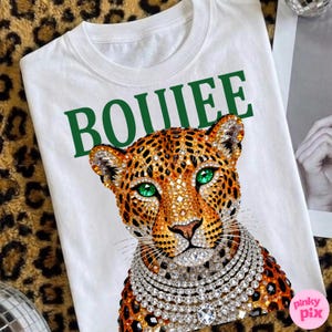 May include: White t-shirt featuring a jeweled leopard design with green eyes and a diamond necklace. The word "BOUIEE" is printed in green above the leopard. The shirt is on a leopard print background.