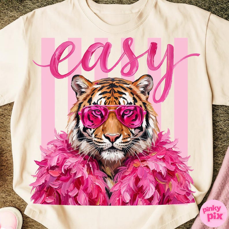 May include: Cream-colored t-shirt featuring a tiger wearing pink sunglasses and a pink feather boa. The word "easy" is written in pink script above the tiger. Pink vertical stripes are behind the tiger.