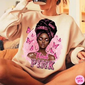 K&ouml;nnte beinhalten: Beiges Sweatshirt mit einer Grafik einer schwarzen Frau mit einem schwarz-rosa Leoparden-Kopftuch und Creolen. Rosa Schmetterlinge und die Worte "Think PINK" sind ebenfalls abgebildet.