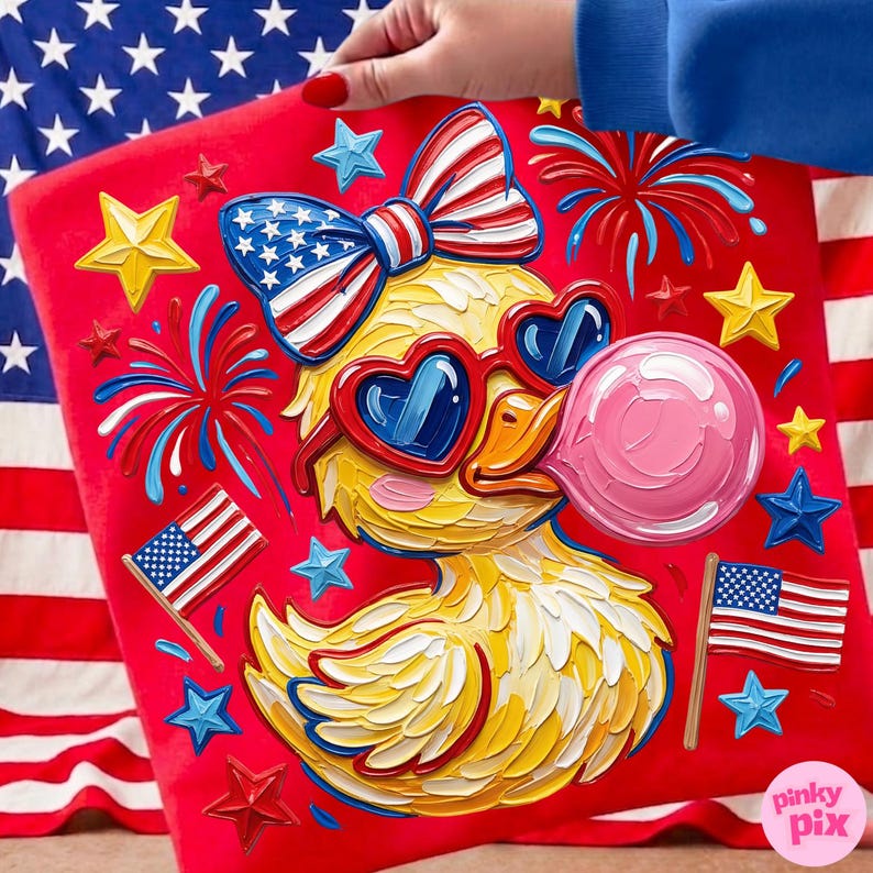May include: A red square pillow featuring a yellow duck wearing heart-shaped sunglasses and blowing a pink bubble. The duck is adorned with a patriotic bow and surrounded by stars, fireworks, and American flags. The pillow is held against an American flag background.