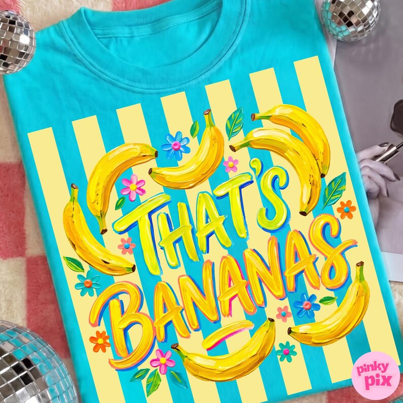 Pu&ograve; includere: Una maglietta turchese con un design a righe gialle e blu. La maglietta presenta la frase "THAT'S BANANAS" in giallo, circondata da illustrazioni di banane gialle, foglie verdi e fiori colorati. Un design divertente e giocoso.