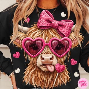 May include: Black sweatshirt featuring a whimsical illustration of a Highland cow with heart-shaped sunglasses and a pink bow. The cow has long, shaggy brown fur and a pink tongue sticking out. Scattered around the cow are pink and white heart accents.