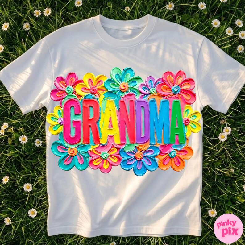 May include: White t-shirt with the word "GRANDMA" in colorful, textured letters, surrounded by vibrant, multi-colored flower designs. The shirt is made of a soft material and is perfect for a gift.
