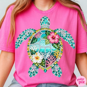 May include: Pink t-shirt featuring a detailed sea turtle design. The turtle is adorned with turquoise and clear gemstones, with a central design of tropical flowers, coral, and ocean scenery. The shirt has a crew neck and short sleeves.