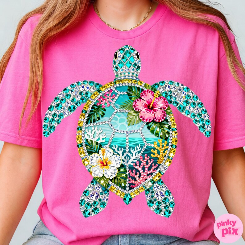 May include: Pink t-shirt featuring a detailed sea turtle design. The turtle is adorned with turquoise and clear gemstones, with a central design of tropical flowers, coral, and ocean scenery. The shirt has a crew neck and short sleeves.