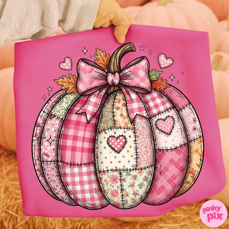 May include: A pink decorative pillow featuring a patchwork pumpkin design. The pumpkin is composed of various pink and floral patterned fabrics, a gingham bow, and heart accents. The pillow is held against a background of pumpkins.