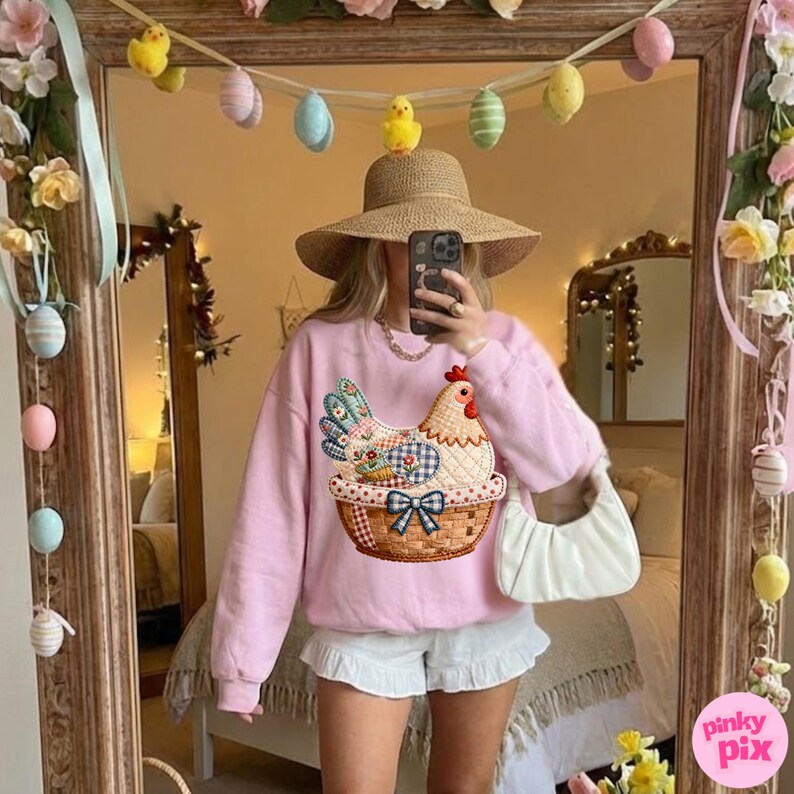 May include: A light pink sweatshirt with a chicken design in a basket. The image is reflected in a mirror decorated with Easter eggs and flowers. The person in the image is wearing a straw hat and white shorts.
