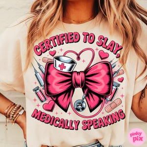 May include: Beige t-shirt with a graphic design featuring a large pink bow, medical equipment, and the text "CERTIFIED TO SLAY, MEDICALLY SPEAKING" in pink. The design includes a nurse's hat, syringes, and hearts.