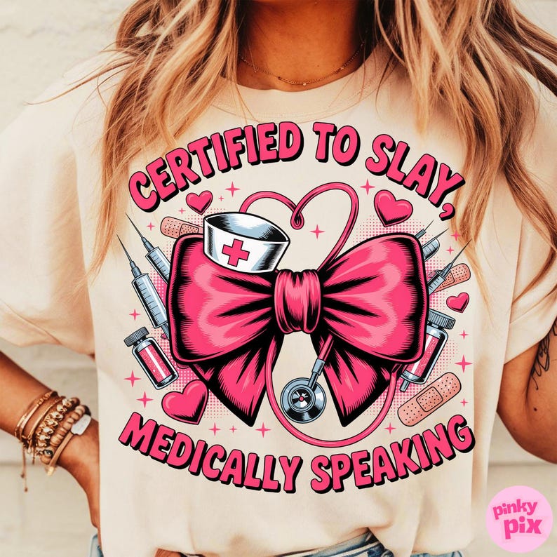 May include: Beige t-shirt with a graphic design featuring a large pink bow, medical equipment, and the text "CERTIFIED TO SLAY, MEDICALLY SPEAKING" in pink. The design includes a nurse's hat, syringes, and hearts.