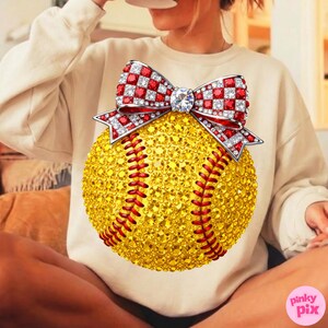 May include: A yellow softball design with red stitching and a sparkling bow. The bow features red and white chequered sections and a large central gem. The softball is covered in small, sparkling gems.